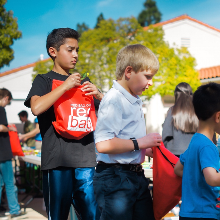 Two boys filling Red Bags at an outdoor table