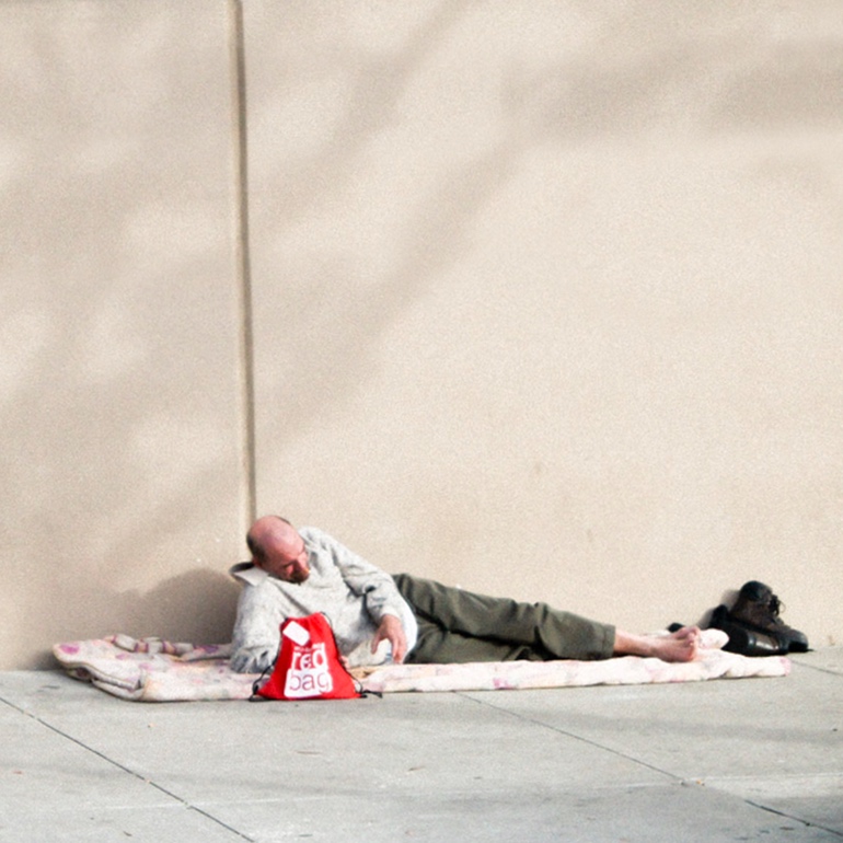 A man asleep on a sidewalk with a Red Bag beside his head