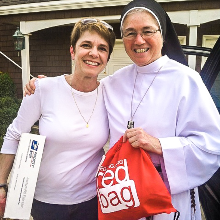 A woman and a nun smiling and holding Red Bags