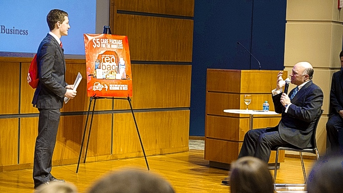 Michael pitching the Red Bag on stage beside a poster, with Kevin O’Leary seated to the right