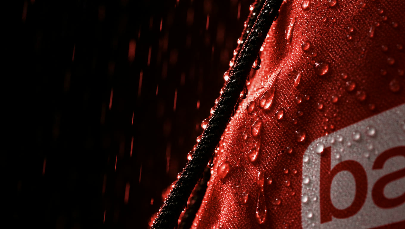 Rain beading on red fabric and a black drawstring, with part of the white logo at the edge